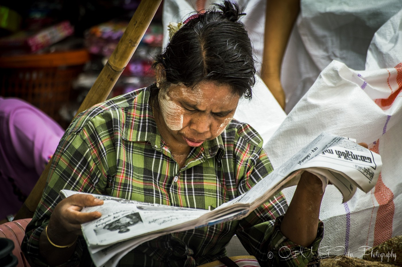 仰光3天:脸颊上涂着thanaka膏的女子正在看当地报纸。仰光,缅甸